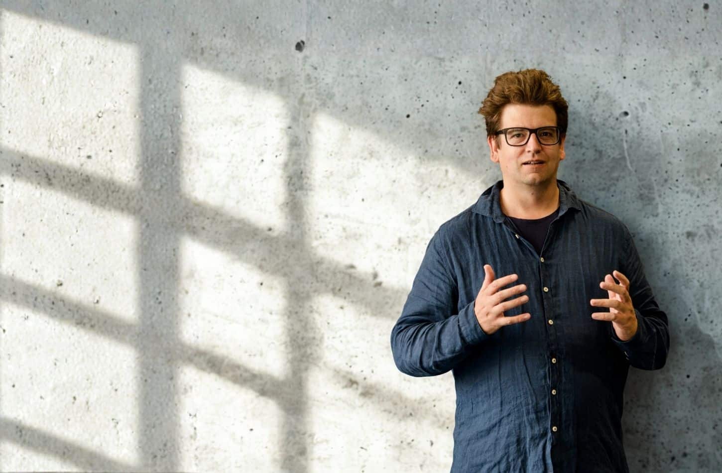 Christoph Galette steht vor einer Betonwand im Sonnenlicht